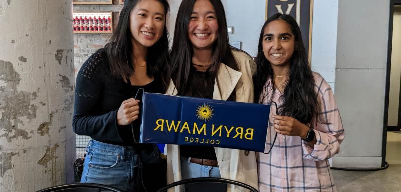 Three GOLD alums pose with a blue banner that says Bryn Mawr College.